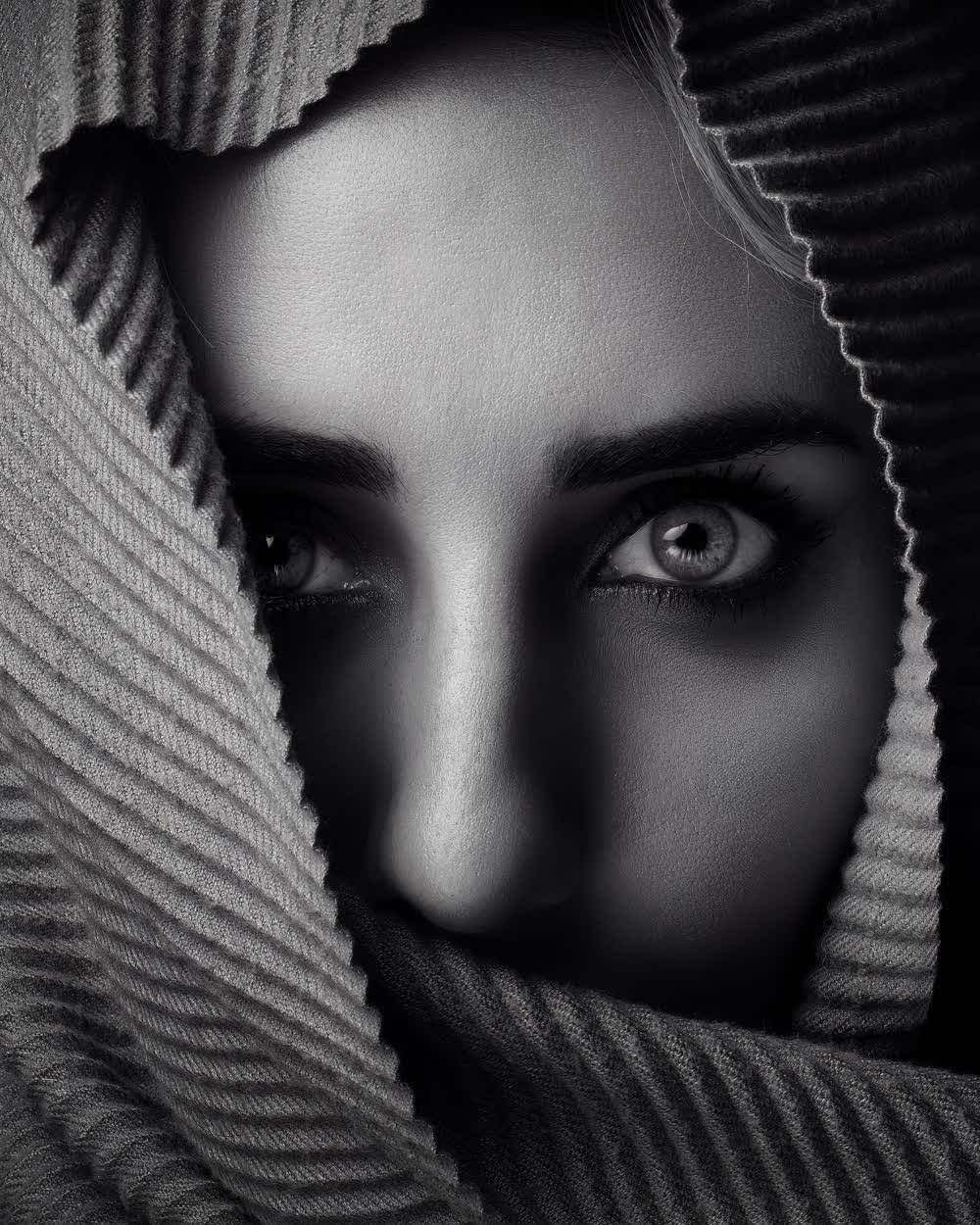 Retrato en blanco y negro, rostro enmarcado por una tela plisada