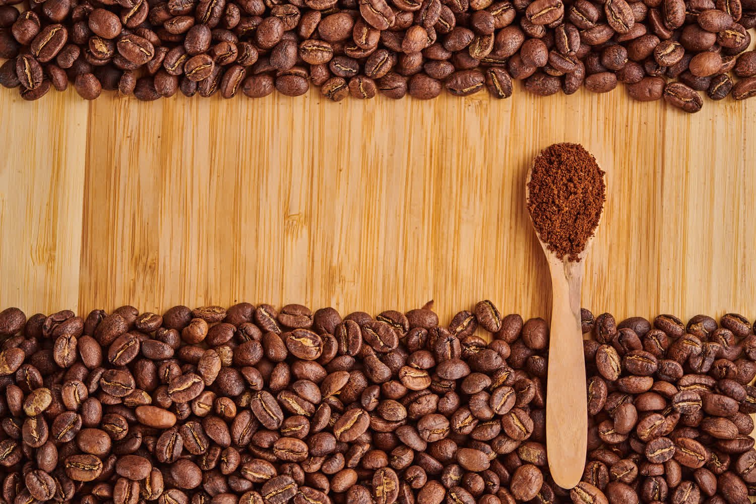 Cuchara con café molido sobre tabla, enmarcada por granos