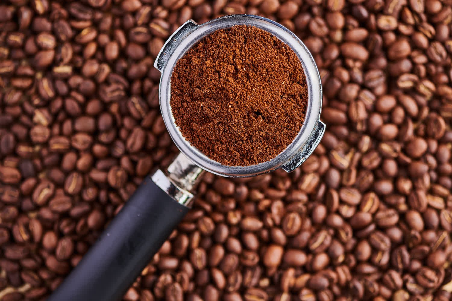 Portafiltro con café molido sobre un lecho de granos