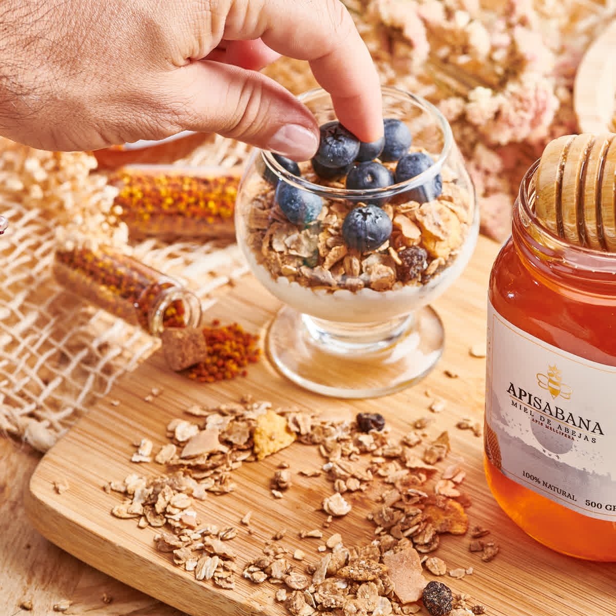 Una mano colocando arándanos sobre una copa de granola