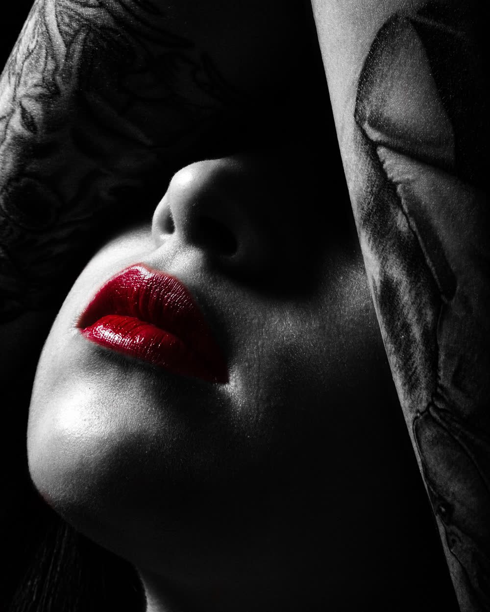 Retrato cerrado en clave baja, monocromo salvo los labios en rojo