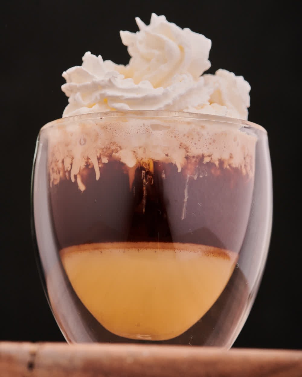 Vaso de café en capas con la crema desbordando, sobre fondo negro